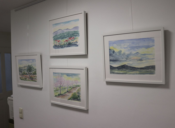 Vier gerahmte Landschaftsaquarelle hängen an einer weißen Wand in einem modernen Praxisraum