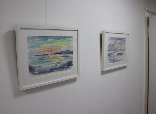 Zwei gerahmte Aquarellbilder mit Landschaftsmotiven hängen an einer weißen Wand neben einer Tür