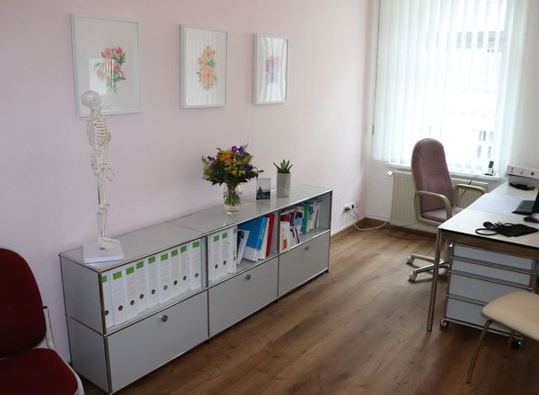 Helles Praxisbüro mit weißen Modulschränken, Schreibtisch am Fenster und anatomischem Skelettmodell an der Wand